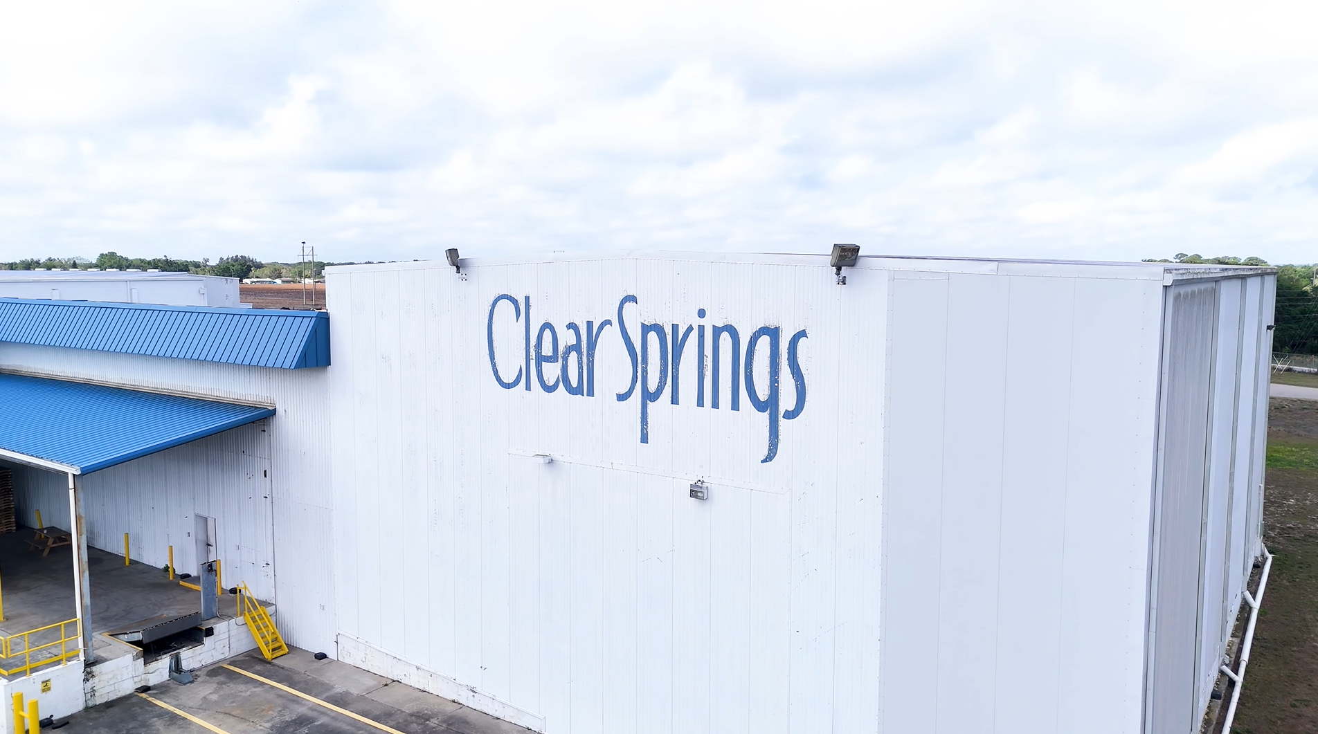 Exterior view of the Clear Springs facility, featuring a blue roof and large white building with the company name prominen...